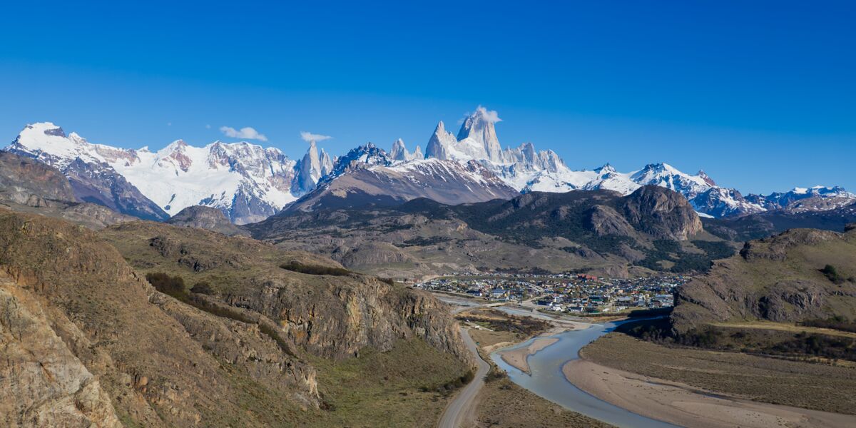 Aerial view of El Chaltén by the De las Vueltas River, at the foot of the snow-capped Cerro Torre and Fitz Roy, with the road reaching the village