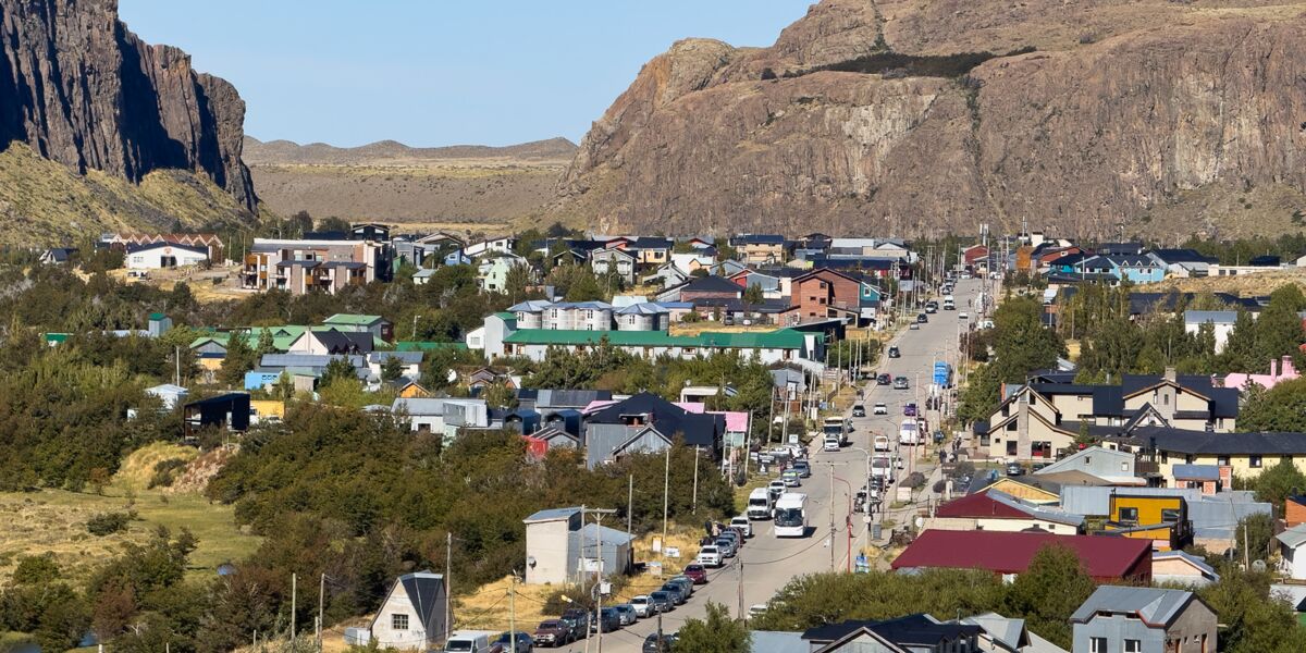El Chaltén seen from above: San Martín Avenue with cars and a bus, houses with colorful roofs and rock walls behind