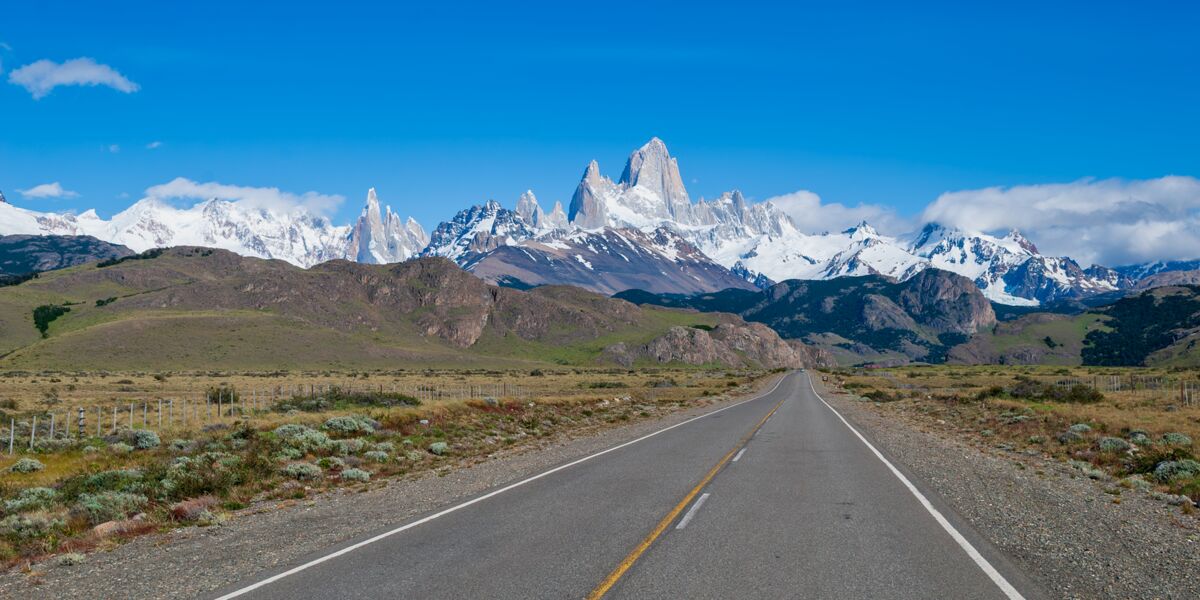 Paved Provincial Route 41 crossing the steppe toward the snow-capped Cerro Torre and Fitz Roy under a blue sky